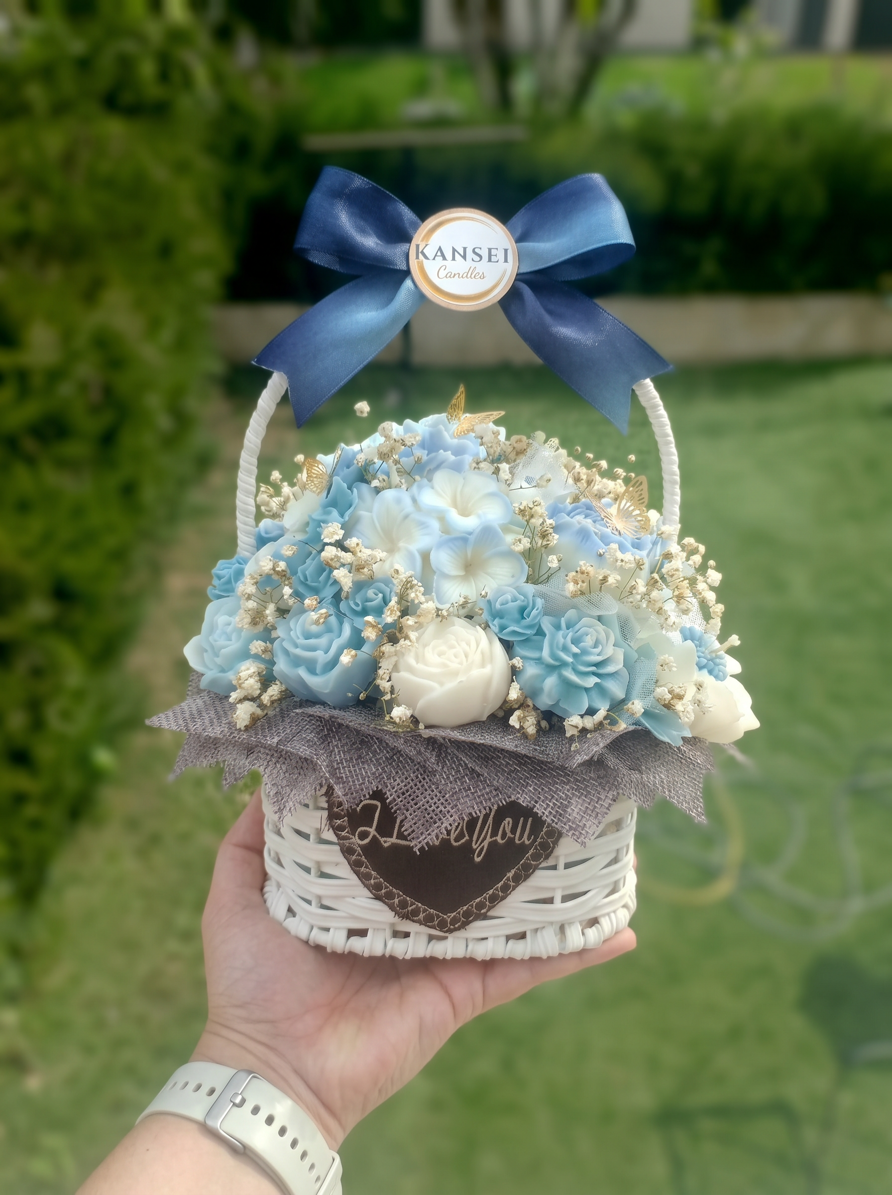 Bouquet Esencial Shizuku de flores de cera azul agua y marfil en cesta blanca con lazo azul